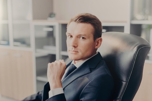 Plan intérieur d'un homme d'affaires sérieux et confiant pose sur une chaise pose au cabinet attend que ses collègues discutent des principaux problèmes de travail Un jeune réalisateur en costume formel réfléchit à un nouveau projet