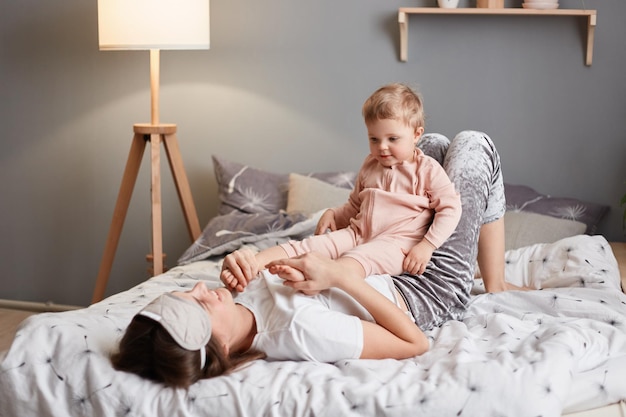 Plan intérieur d'une mère et d'un enfant se câlinant ensemble sur un lit douillet heureux beau bébé adorable aux pieds nus portant un dormeur rose jouant avec maman dans la chambre en profitant d'un matin heureux