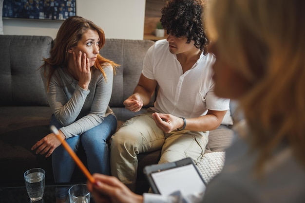 Photo plan d'un jeune couple ayant une discussion lors d'une séance de conseil avec leur psychothérapeute alors qu'il est assis sur un canapé à l'intérieur d'un salon.