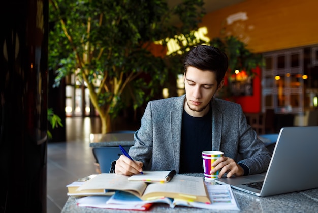 Plan d'un jeune étudiant assis à table et écrivant sur un cahier. Jeune étudiant étudiant au café.