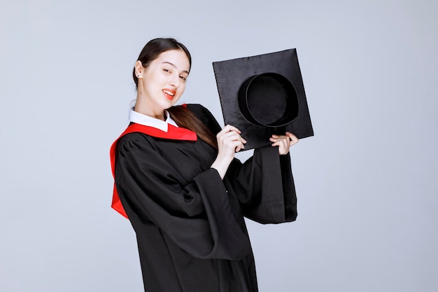 Plan d'une jeune étudiante en toge montrant sa casquette de fin d'études. photo de haute qualité