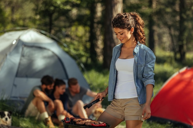 Plan d'une jeune femme faisant un barbecue en camping avec des amis