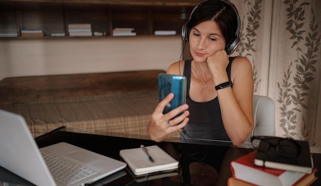 Plan d'une jolie jeune femme utilisant son téléphone portable tout en travaillant avec un ordinateur portable assis à la maison