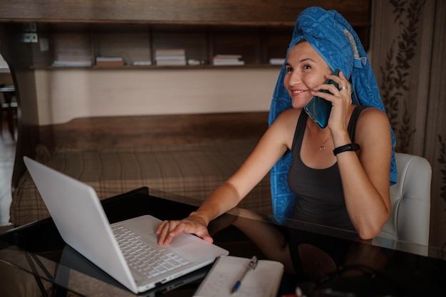 Plan d'une jolie jeune femme utilisant son téléphone portable tout en travaillant avec un ordinateur portable assis à la maison