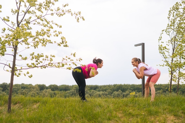 Plan large d'une entraîneuse de fitness joyeuse donnant une formation personnelle à une jeune femme motivée en surpoids en plein air en été L'instructeur aide une grosse femme à perdre du poids à l'extérieur en faisant des squats à l'extérieur