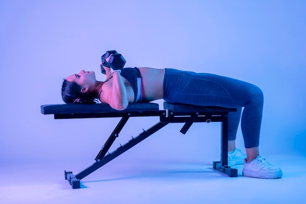 Plan latéral d'un banc de femme pressant avec deux haltères