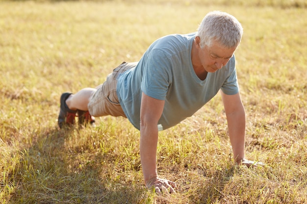 Plan d'un mâle mature qui pousse sur l'herbe verte, est flexible, se réchauffe avant de faire du jogging, aime l'air frais et la belle nature, prend soin du corps. Ambiance sportive. Pensionné a une séance d'entraînement dans la campagne