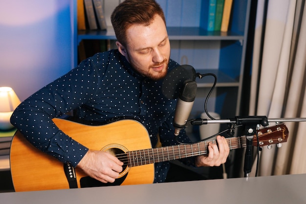 Plan moyen d'un chanteur guitariste talentueux jouant de la guitare acoustique et chantant dans un microphone enregistrant une chanson dans un home studio