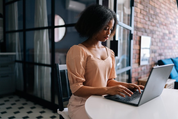 Plan moyen d'une étudiante africaine sérieuse en train de taper sur un clavier d'ordinateur portable étudiant en ligne Femme d'affaires noire travaillant sur un ordinateur portable au bureau