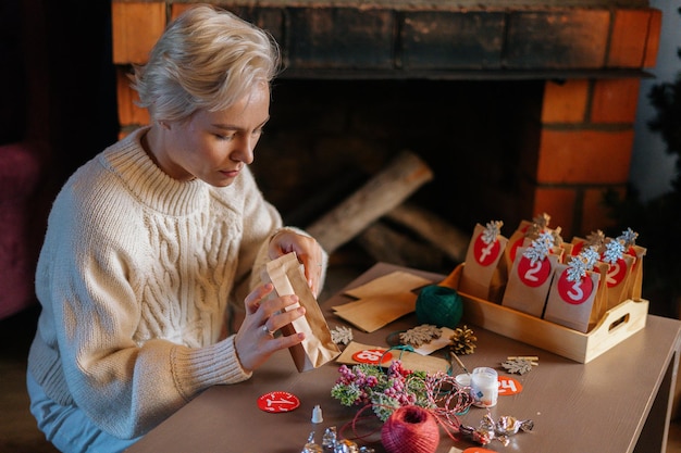 Plan moyen d'une jeune femme mettant des bonbons dans un sac de calendrier de l'Avent de Noël la veille de Noël assis par