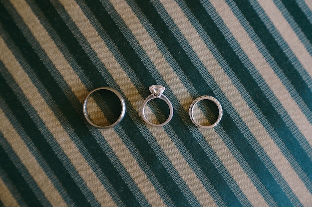 Plan rapproché des anneaux de mariage d'or blanc et d'une bague de fiançailles de pierre gemme pour une jeune mariée sur le tissu bleu avec