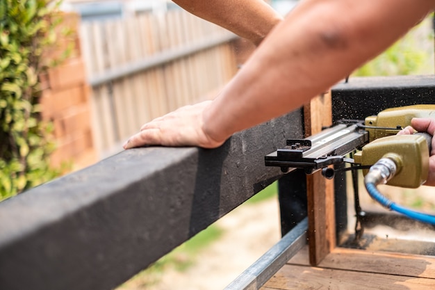 Plan rapproché d'un charpentier d'homme de main utilisant le pistolet à clous d'air pour compléter la table en bois dans le jardin