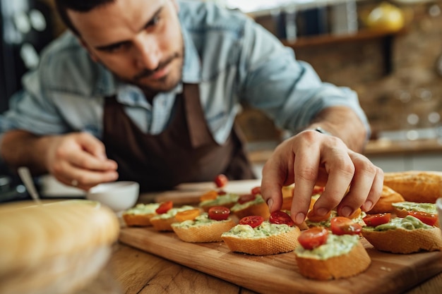 Plan rapproché du chef ajoutant la tomate cerise sur le dessus de la bruschetta tout en préparant la nourriture dans la cuisine