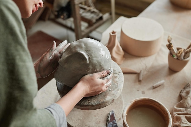 Plan rapproché du concepteur faisant la sculpture du visage humain de l'argile dans le studio en céramique