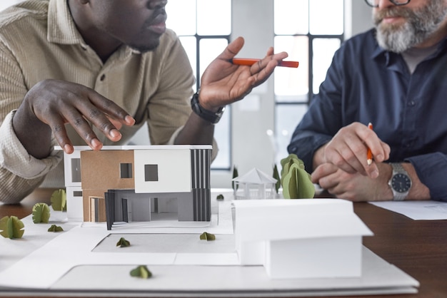 Photo plan rapproché du modèle de carton du nouveau bâtiment sur la table avec deux architectes se parlant à l'arrière-plan