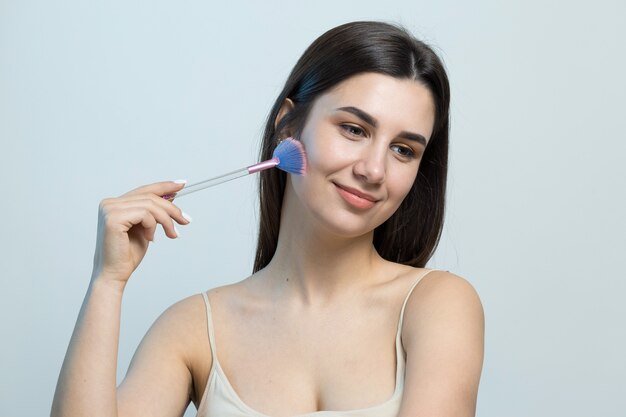 Plan rapproché d'une jeune fille dans un dessus léger sur un fond blanc faisant un maquillage facial