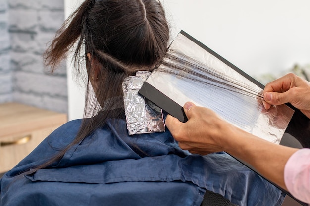 Plan rapproché des mains d'un artiste dans un salon de coiffure professionnel colorant les cheveux de son client