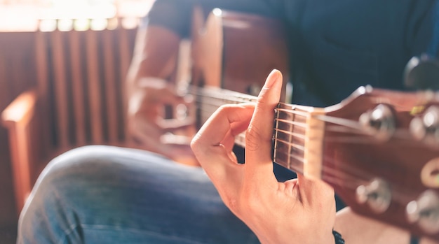 Plan rapproché des mains et des doigts d'un musicien masculin jouant une guitare acoustique