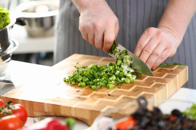 Plan rapproché des mains du cuisinier tenant le couteau pour couper les oignons verts