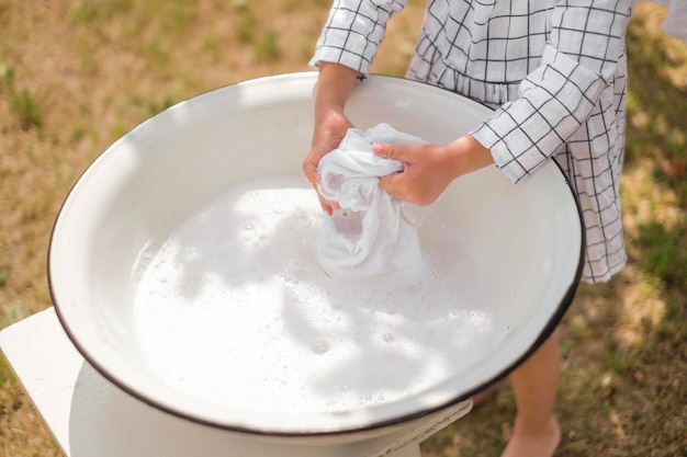 Plan rapproché des mains des enfants lavant une chemise blanche comme neige dans un bassin