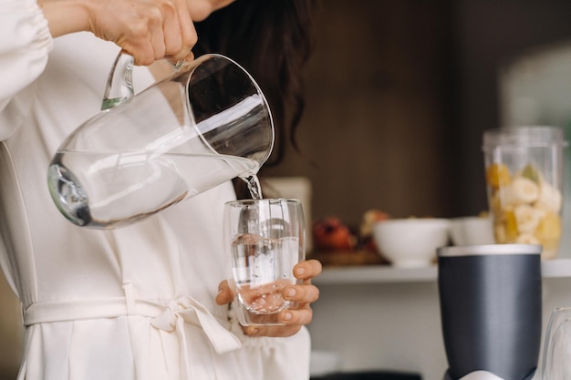 Plan rapproché des mains d'une fille dans la cuisine qui verse de l'eau propre dans un verre