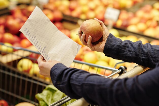 Plan rapproché des mains mûres de client tenant la liste d'achats et la pomme