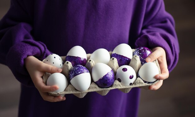 Plan rapproché d'un plateau des oeufs de pâques pourpres dans les mains d'un enfant