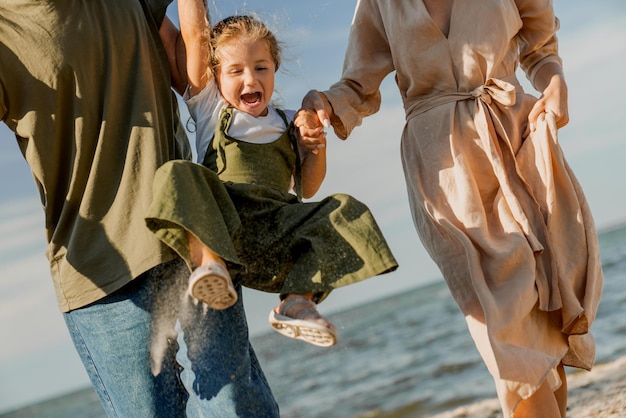 Plan recadré d'une famille heureuse marchant et s'amusant sur la plage avec une jolie fille heureuse