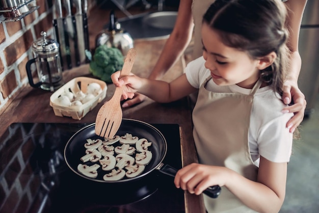 Plan recadré de la fille et de la mère faisant frire des champignons sur la cuisinière ensemble pour le dîner à la cuisine