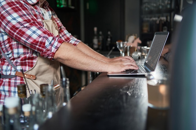 Photo plan recadré d'un jeune barista prenant des notes et utilisant un ordinateur portable