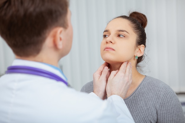 Photo plan recadré d'une jeune femme qui se fait examiner le cou et la gorge par un médecin de l'hôpital.