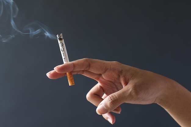 Plan recadré de la main humaine fumant une cigarette isolée sur fond gris