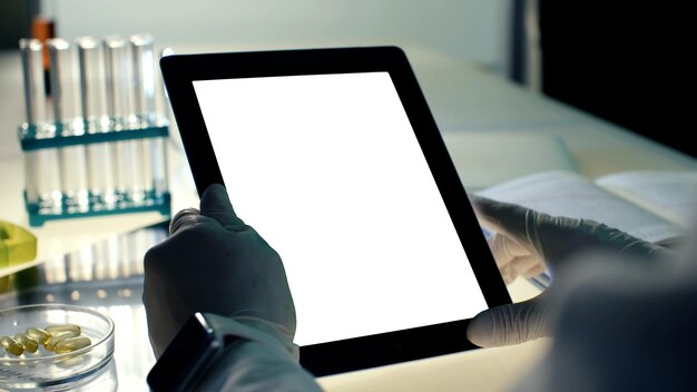 Photo plan recadré d'un médecin en gants à l'aide d'une tablette pc avec écran blanc vierge dans un laboratoire moderne
