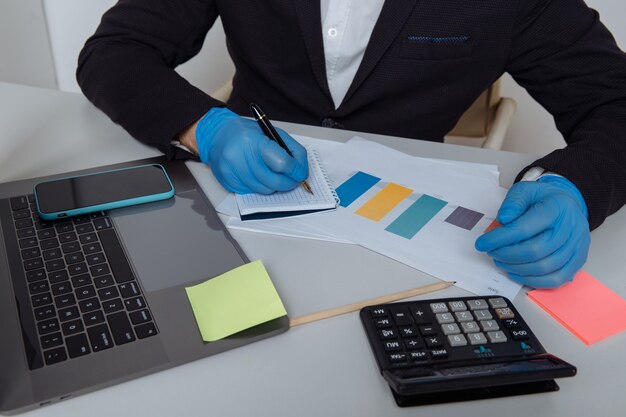 Plan recadré d'un travailleur portant des gants de protection calculant un rapport alors qu'il travaillait au bureau.