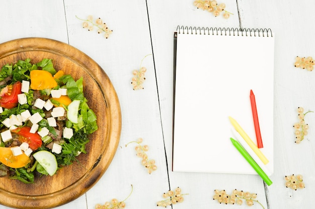 Plan de régime une salade de légumes frais et un cahier vierge sur une table en bois blanche