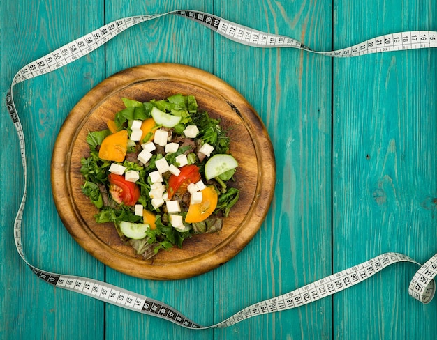 Plan de régime salade de légumes frais et ruban à mesurer sur une table en bois blanc