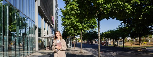 Photo plan vertical d'une femme d'affaires marchant dans la rue avec une tablette numérique allant au travail portant du beige