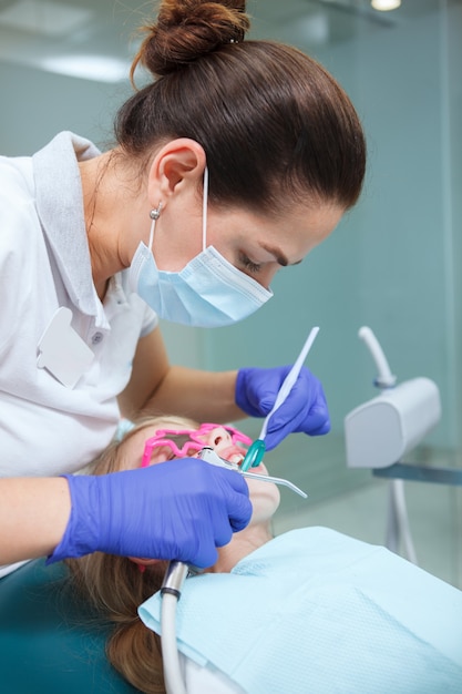 Plan vertical d'une femme dentiste portant un masque médical, travaillant avec un enfant patient