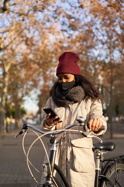Plan vertical d'une femme faisant du vélo à l'aide de son smartphone. Elle porte des vêtements d'hiver et se trouve dans une ville avec un temps d'automne.