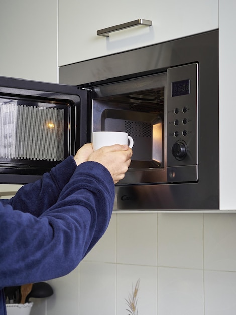 Photo plan vertical d'un homme mettant une tasse au micro-ondes