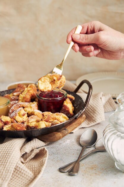 Plan vertical d'une main tenant une fourchette avec une trempette kaiserschmarrn dans de la purée de pommes sur une table