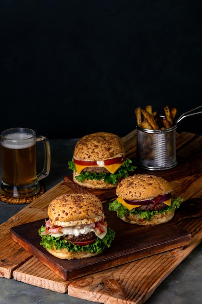 Plan vertical de trois hamburgers sur une planche en bois à côté d'une cruche de bière et de quelques frites