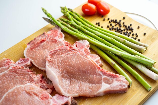 Une planche de bois avec des asperges de côtelettes de porc et des tomates cerises