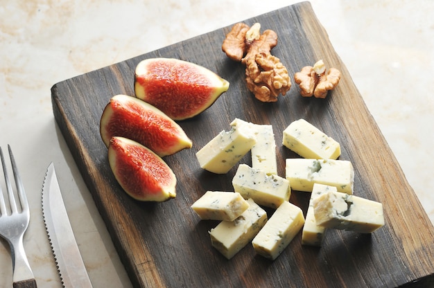 Sur une planche de bois, du fromage avec de la moisissure bleue dorblu, quelques figues et des noix.