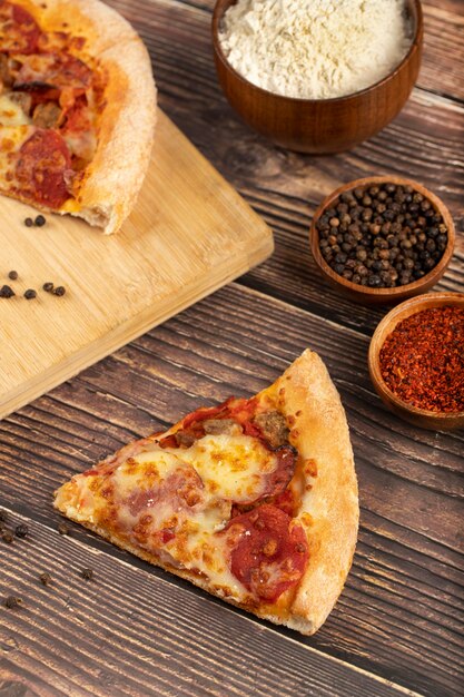 Planche de bois de pizza en tranches avec du poivre de Cayenne et des grains de poivre sur la table.