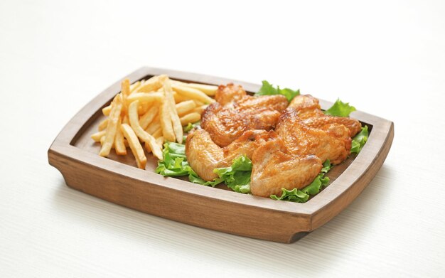 Planche de bois avec poulet savoureux et frites sur table