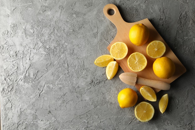 Planche, citrons et presse-agrumes sur surface grise. Fruits mûrs