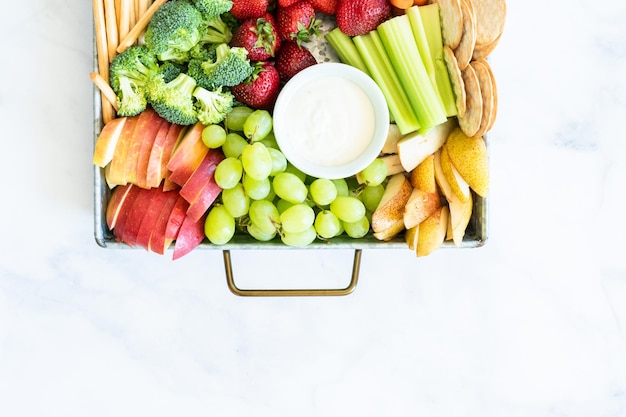 Planche de collations avec des fruits frais, des légumes, des craquelins et des trempettes.