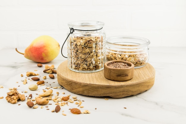 Planche de cuisine avec bocaux en verre remplis de muesli ou de granola pour faire de l'avtraka. noix, poire mûre pour améliorer le goût. alimentation équilibrée.