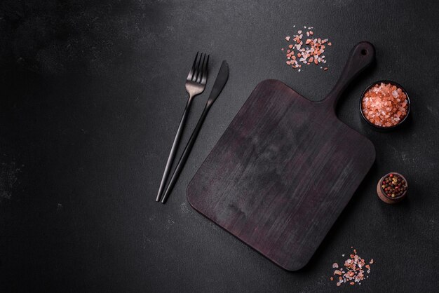 Planche à découper en bois avec appareils de cuisine sur fond de béton noir